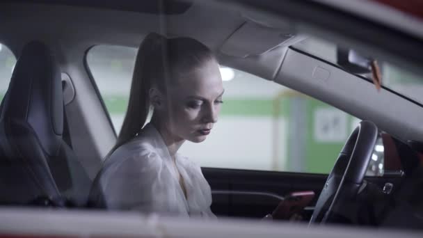 Mulher elegante na camisa branca senta-se no carro, mantém o volante ao lado da garagem — Vídeo de Stock