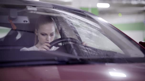 Mooie vrouw in wit overhemd zit in de rode auto en houdt van stuurwiel in garage — Stockvideo