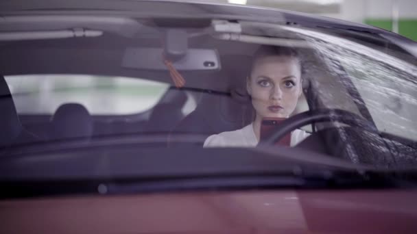 Atractiva mujer vestida con camisa blanca se sienta en coche rojo detrás del volante — Vídeos de Stock
