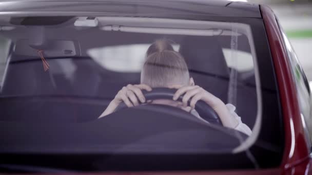 Desperate female with ponytail sits in red car and puts head on steering wheel — Stock Video