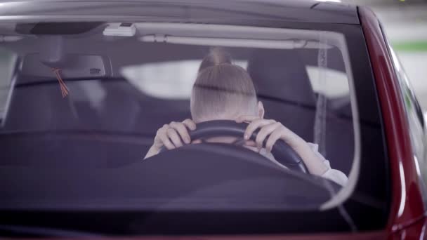 Young woman with ponytail sits in red car and puts head on steering wheel — Stock Video