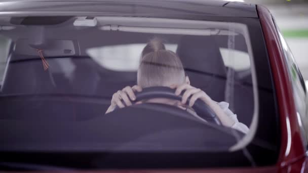 Desperate woman with ponytail sits in red car and puts head on steering wheel — Stock Video