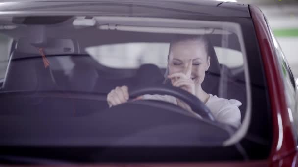 Vue de la femme à queue de cheval assise dans une voiture rouge et souriant derrière le volant — Video