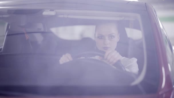 View of girl with ponytail sitting in red car and smiling behind steering wheel — Stock Video