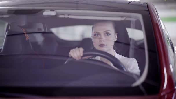 Όμορφο κορίτσι σε λευκό πουκάμισο κάθεται σε κόκκινο αυτοκίνητο και κοιτάζοντας γύρω στο γκαράζ — Αρχείο Βίντεο