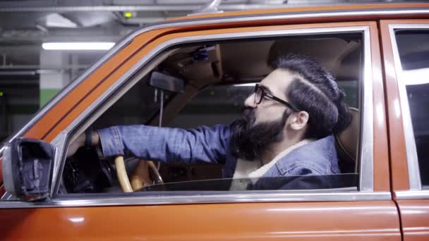 Mature bearded guy with long dark hair closes red car window and looks out of it — Stock Video