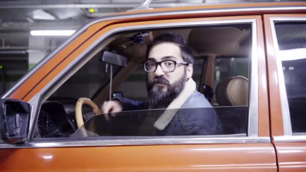 Hombre barbudo guapo con el pelo largo abre la ventana roja del coche y comienza a hablar . — Vídeos de Stock