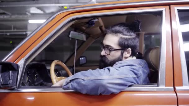 Hosszú haj vonzó szakállas férfi ül a piros autó, és úgy néz ki, ablakon — Stock videók