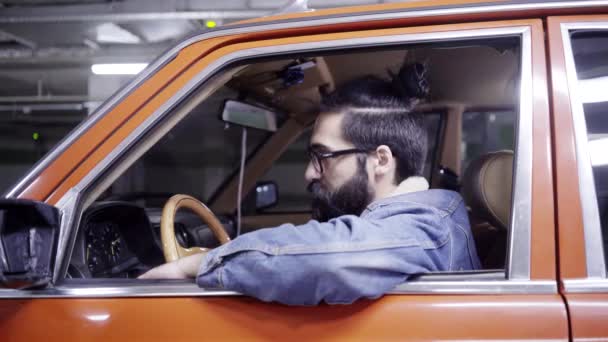 Attraente maschio barbuto con i capelli lunghi guarda fuori dal finestrino dell'auto e guida via — Video Stock