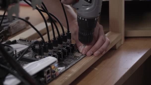 Las manos de los hombres usan un destornillador electrónico para conectar la placa base a la plancha de madera — Vídeo de stock