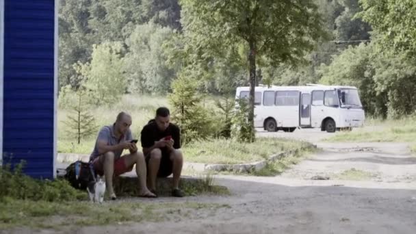 Deux hommes matures assis sur le trottoir en regardant leurs smartphones à la banlieue . — Video