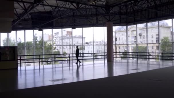 Большой пустой зал с высоким потолком, где человек ходит в темном костюме говорит по телефону — стоковое видео