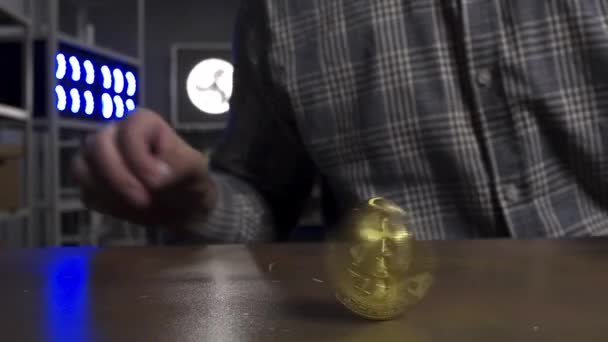 Funny man in sunglasses joyfully spins big new gold bitcoin coin on brown table. — Stock Video