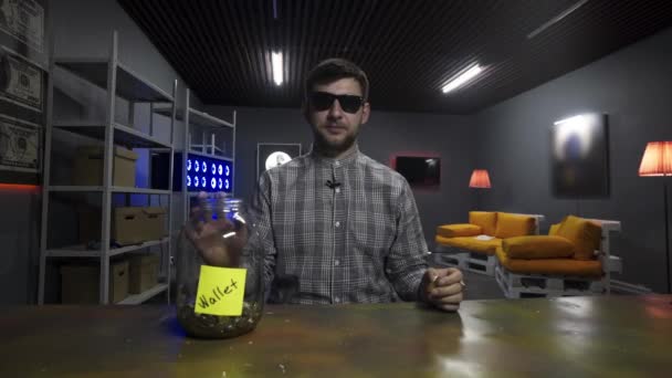 Engraçado jovem blogueiro cai grande bitcoin ouro em frasco de vidro na frente da câmera — Vídeo de Stock