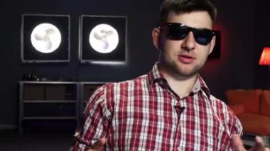 Güneş gözlüğü takan yakışıklı sakallı adam gülümsüyor, konuşuyor ve kameraya bakıyor