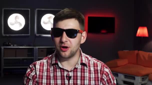 Nice-looking young man wearing sunglasses smiles, speaks and looks at camera — Stock Video