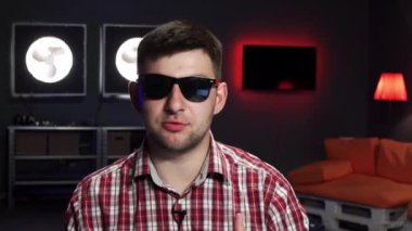 Güneş gözlüğü takan beyaz sakallı adam gülümsüyor, konuşuyor ve kameraya bakıyor