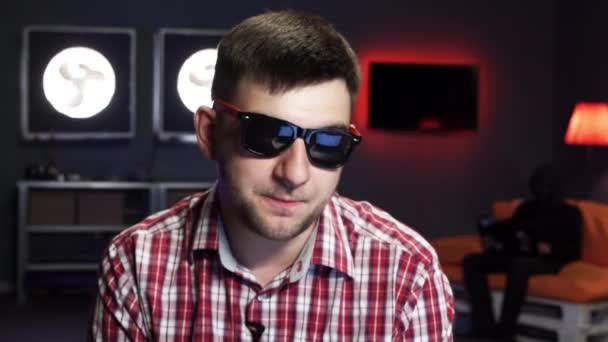 Homem com óculos de sol emocionalmente fala s na câmera enquanto alguém se senta no sofá — Vídeo de Stock