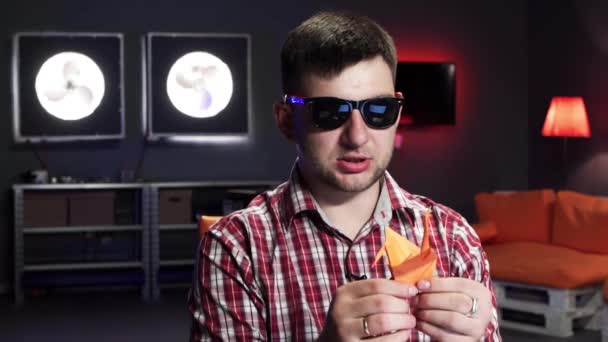 Aantrekkelijke bebaarde kerel met zonnebril is vouwen schattig oranje origami kraan. — Stockvideo