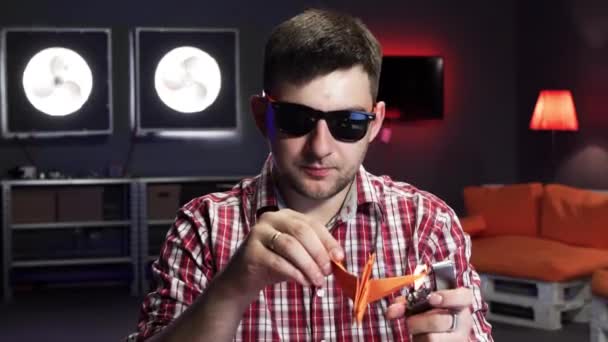 Guapo barbudo con gafas de sol pone en fuego plegado grúa de origami naranja — Vídeo de stock