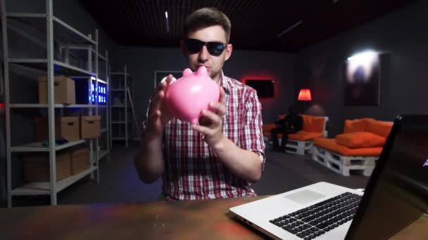 Cute bearded man with sunglasses holds plastic pig, speaks and looks at camera — Stock Video