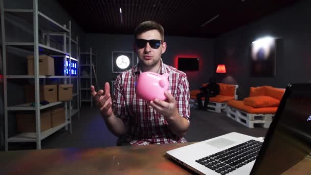 Mann mit Sonnenbrille spricht und blickt in Kamera mit Sparschwein in der Hand — Stockvideo