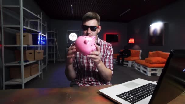 Funny bearded man with sunglasses holds plastic pig, speaks and looks at camera — Stock Video