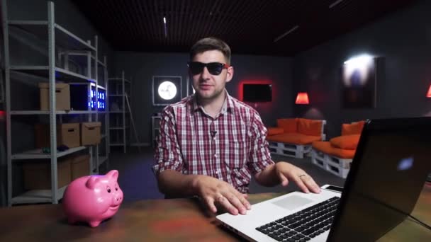 Enthusiast mit Sonnenbrille spricht in die Kamera, Schwein und Laptop auf dem Schreibtisch — Stockvideo