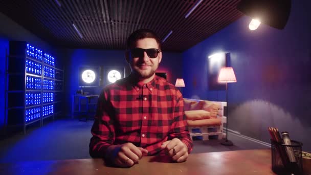 Привлекательный мужчина сидит за столом, показывает взорванный поцелуй в комнате с освещенными холодильниками — стоковое видео