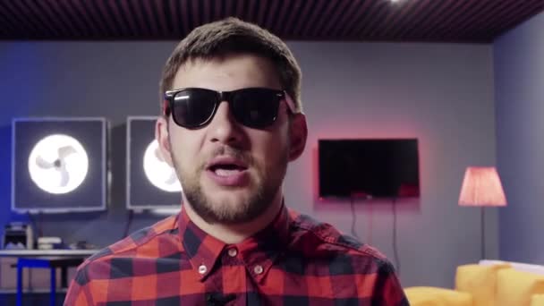 Lustige niedliche junge bärtige Mann mit Sonnenbrille aufgesetzt dynamisch spricht in die Kamera — Stockvideo