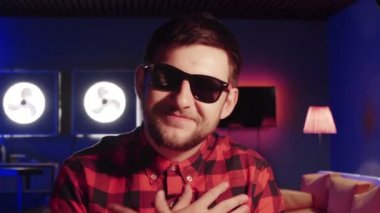 Güneş gözlüğü ile yakışıklı genç erkek kameraya bakar, gülümsüyor, el hareketleri kullanır