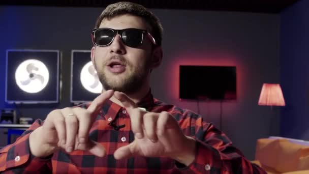 Funny young male with sunglasses looks at camera, smiles, uses hand gestures — Stockvideo