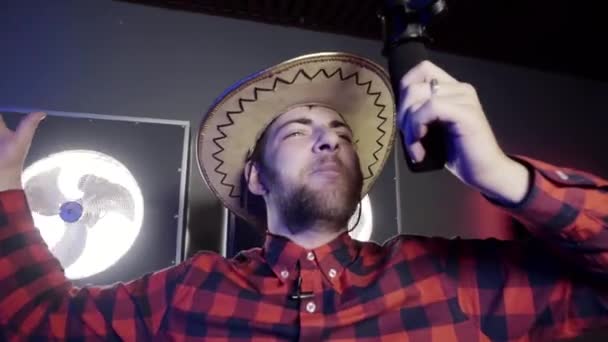 Nice-looking grey eyed bearded man with mexican hat holds microphone and sings. — Stock Video