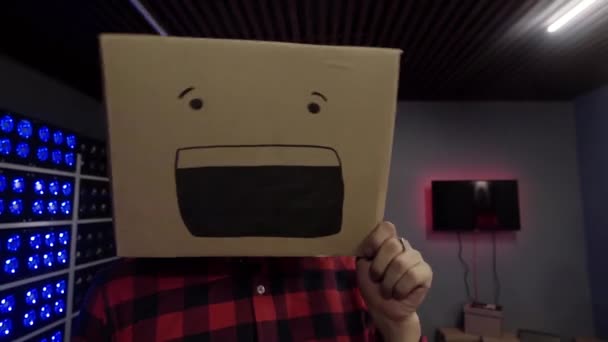 Leuke grappige kerel zet kartonnen doos met getekende glimlach op zijn hoofd bij camera in Studio — Stockvideo