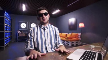 Gülümseyen sakallı adam karanlık odada dizüstü bilgisayar ile masanın arkasında oturan vlogging olduğunu