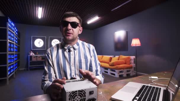 Nice looking young male speaks at camera holding box of power supply with cooler — Stock Video