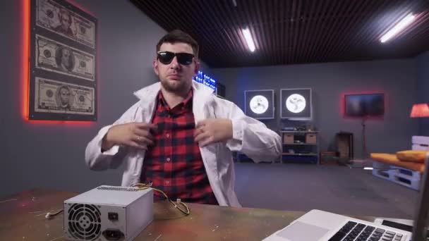 Hombre vistiendo bata de laboratorio blanca se sienta detrás del escritorio con caja de fuente de alimentación con enfriador — Vídeo de stock