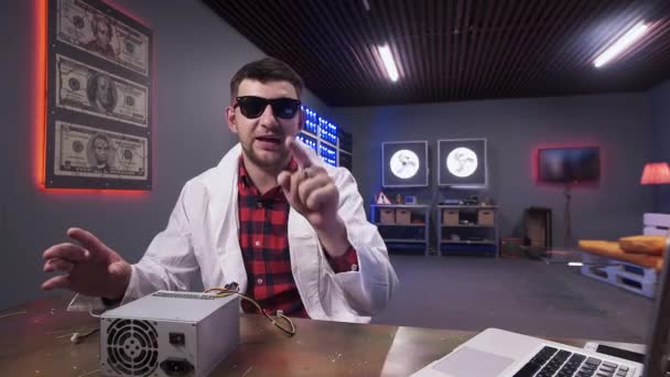 Темноволоса людина в білому лабораторному пальто говорить до камери, що сидить за столом — стокове відео