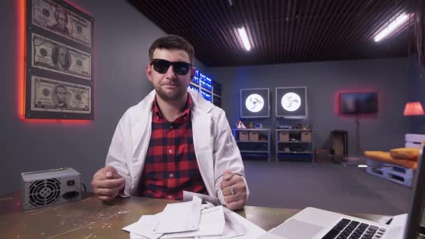 Guy dragen zonnebril en witte Lab vacht spreekt op camera houden enveloppen — Stockvideo