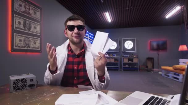 Чоловік в сонцезахисних окулярах і біле лабораторне пальто говорить на камеру, що тримає конверти — стокове відео
