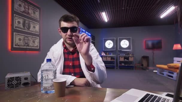 Man wetenschapper dragen Lab Coat zit achter bureau met plastic fles en beker — Stockvideo