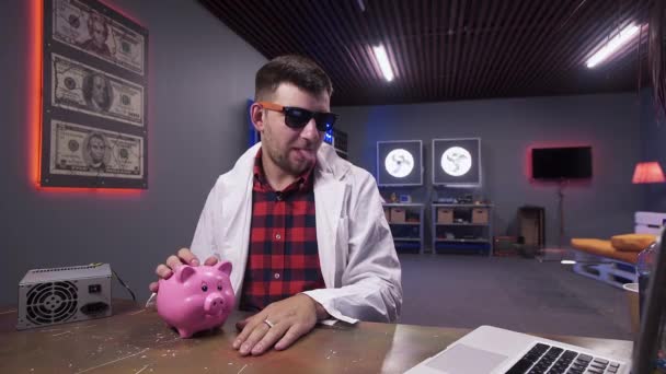 Funny guy wearing sunglasses and lab coat speaks having pig and laptop on desk — Stock Video