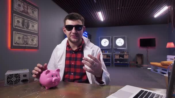 Young man with sunglasses actively speaks at camera put pig and laptop on desk — 비디오