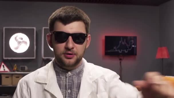 Bearded young man wearing sunglasses and white lab coat is looking at his watch. — Stock Video