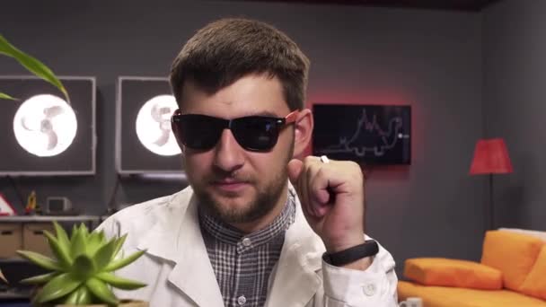 L'uomo che indossa occhiali da sole e camice da laboratorio bianco parla tenendo pot con pianta . — Video Stock