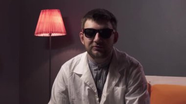 Güneş gözlüğü ve beyaz laboratuvar önlüğü giyen sakallı sevimli adam bir şeyleri açıklıyor.