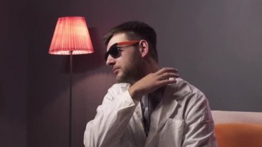 Sakallı güzel görünümlü adam güneş gözlüğü ve beyaz laboratuvar önlüğü toches yaka giyiyor