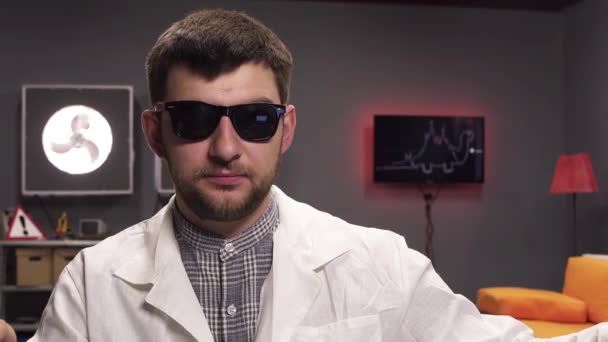 Entusiastisk kille med skägg bär solglasögon och vit labbrock talar. — Stockvideo