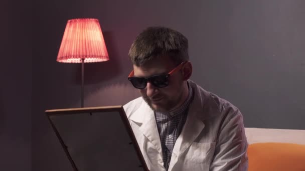 Ελκυστικός τύπος με γένια φορώντας γυαλιά ηλίου και λευκό εργαστήριο κρατά εικόνα στο πλαίσιο — Αρχείο Βίντεο