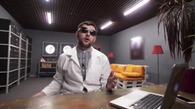 Laboratuvar önlüğü giyen adam soğutucu ile güç kaynağı kutusu tutan kamera konuşuyor.